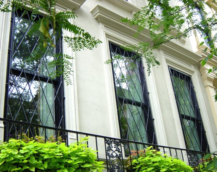 Black diamond lattice guards on tall windows of a cream stone townhouse with green planting