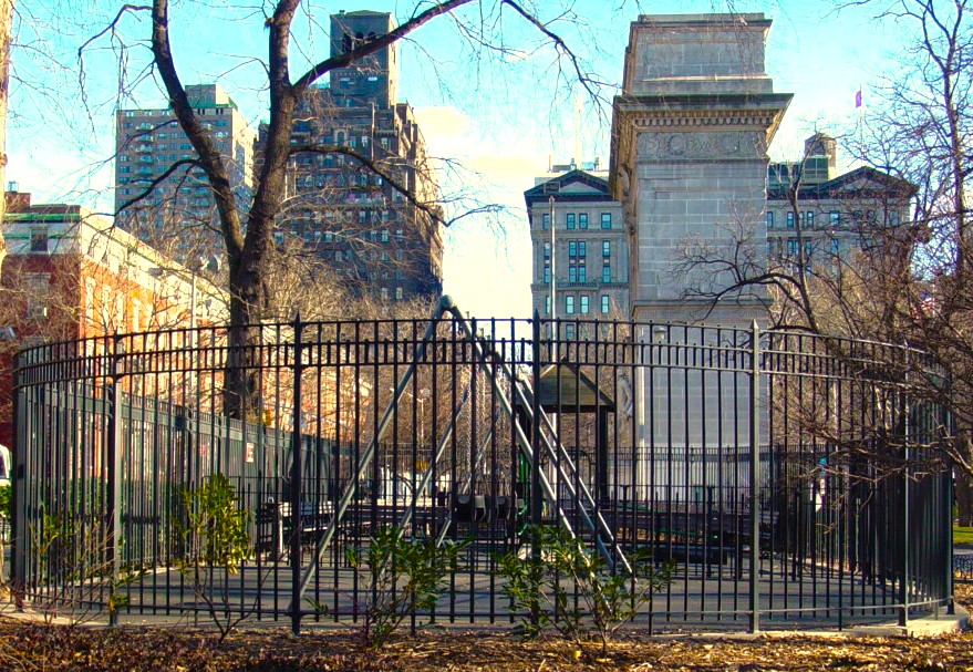 Curved black picket fence around a bare winter playground with city towers behind