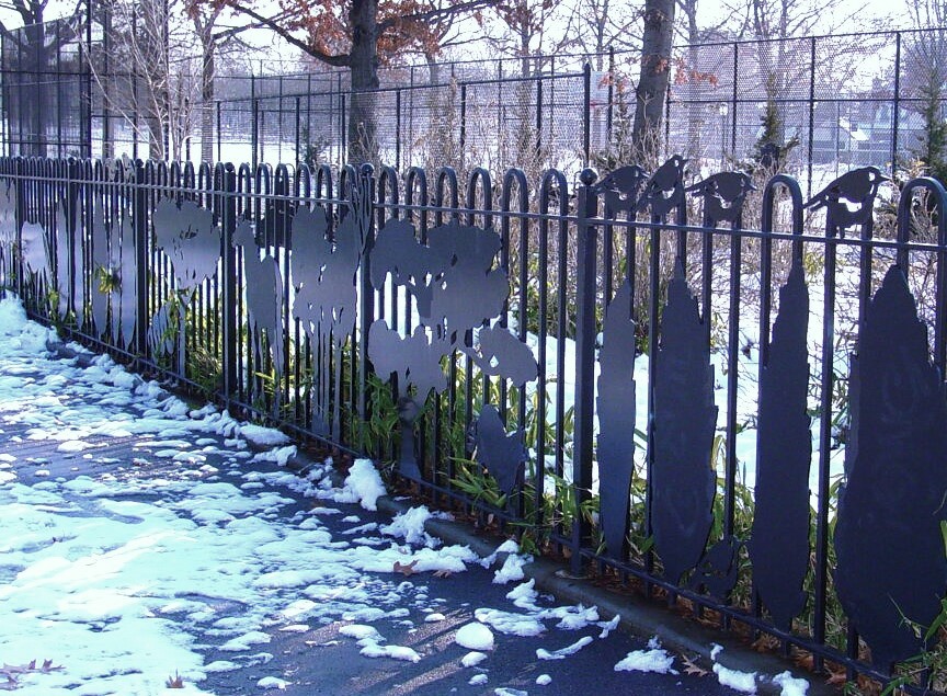 Loop-topped fence with cut leaf and bird silhouettes above a snowy park path