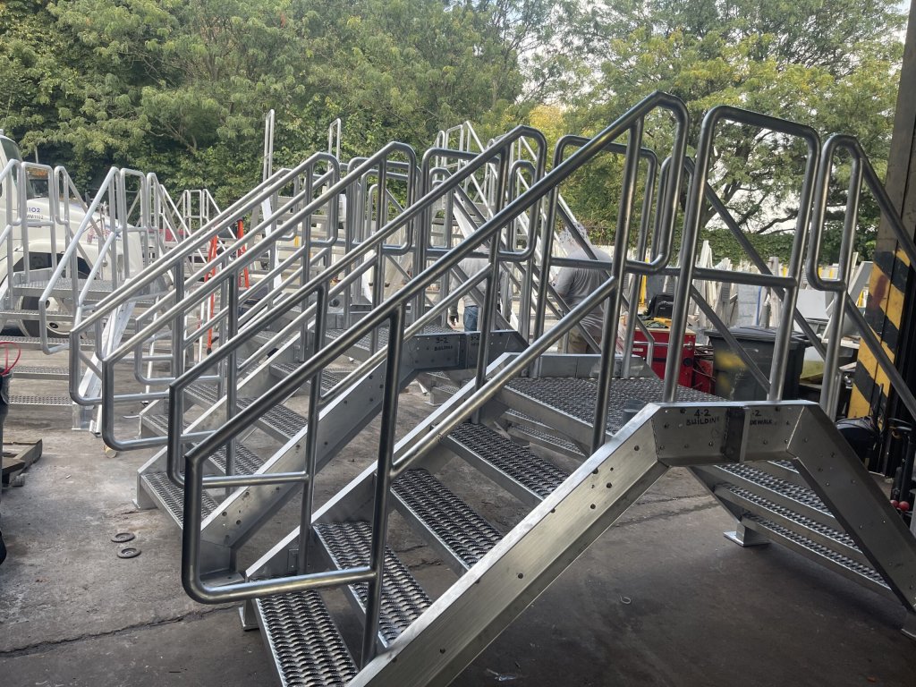 Welded aluminium crossover bridges with tubular handrails standing in a yard under green trees
